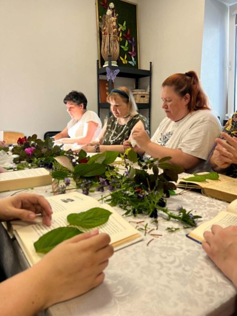 Bendruomenės narės dėlioja gėles ir lapus džiovinimui