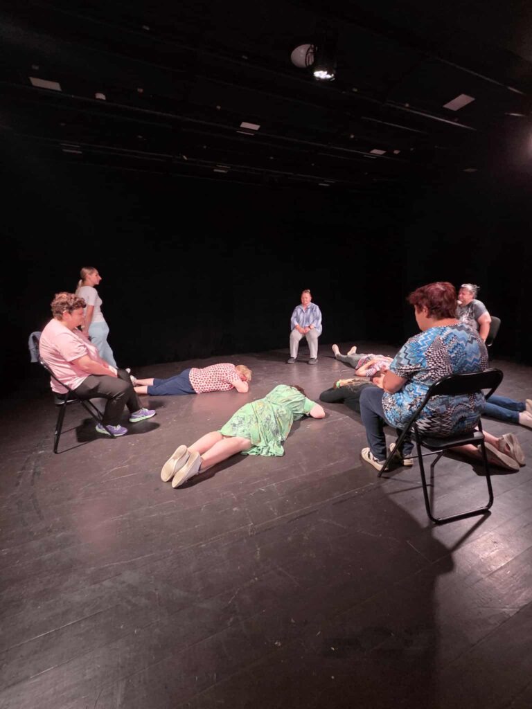 A theatre performer is lying on stage during a creative exercise